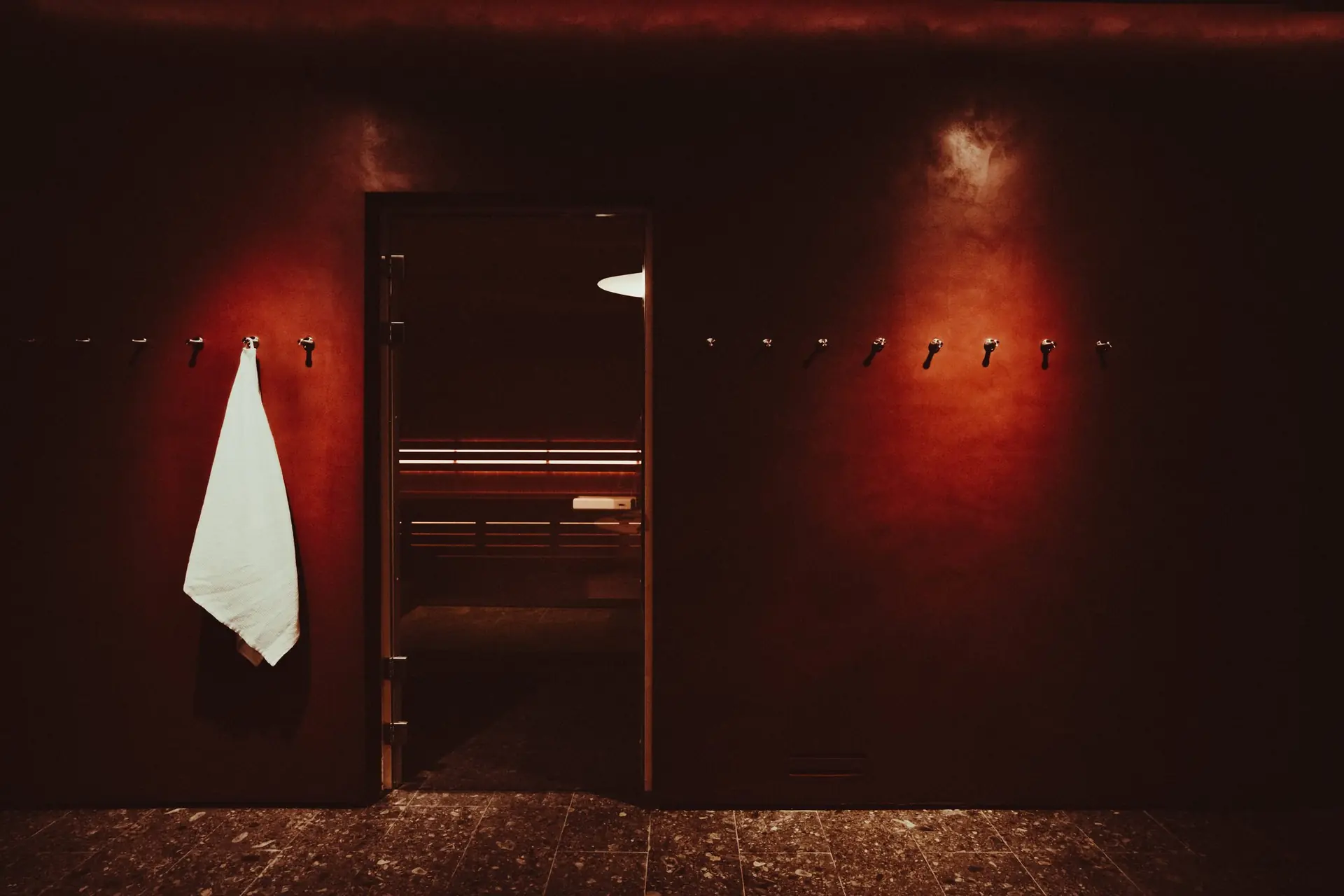 Vestiaire rouge, patères en laiton, serviette blanche, porte vitrée du sauna