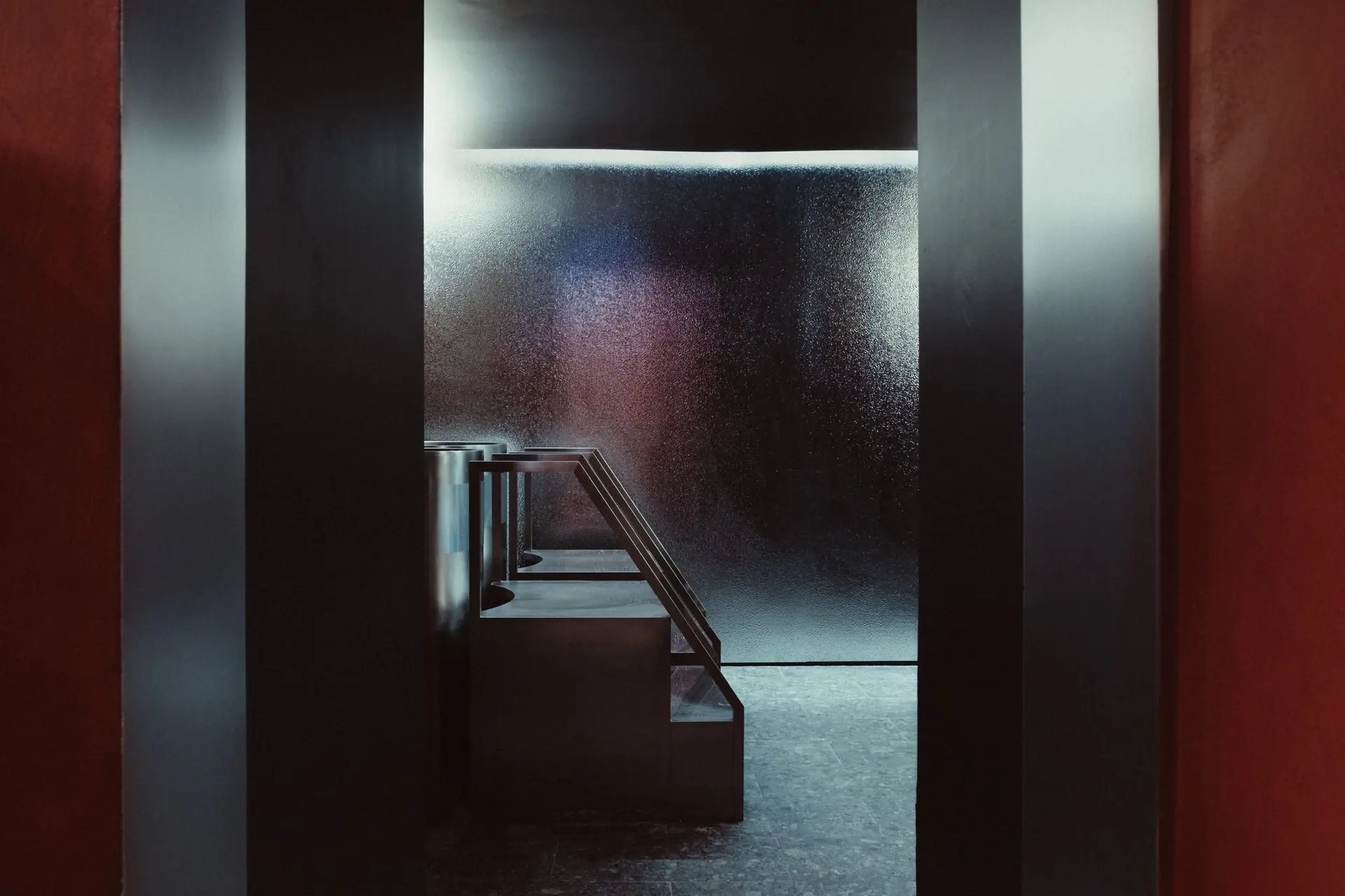 Enfilade de portes vers une salle éclairée, vasques en métal, terrazzo